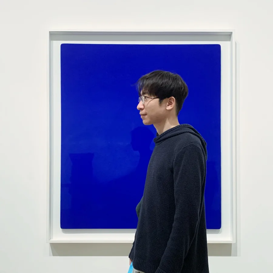 Qian Zhao standing in front of a vivid blue artwork